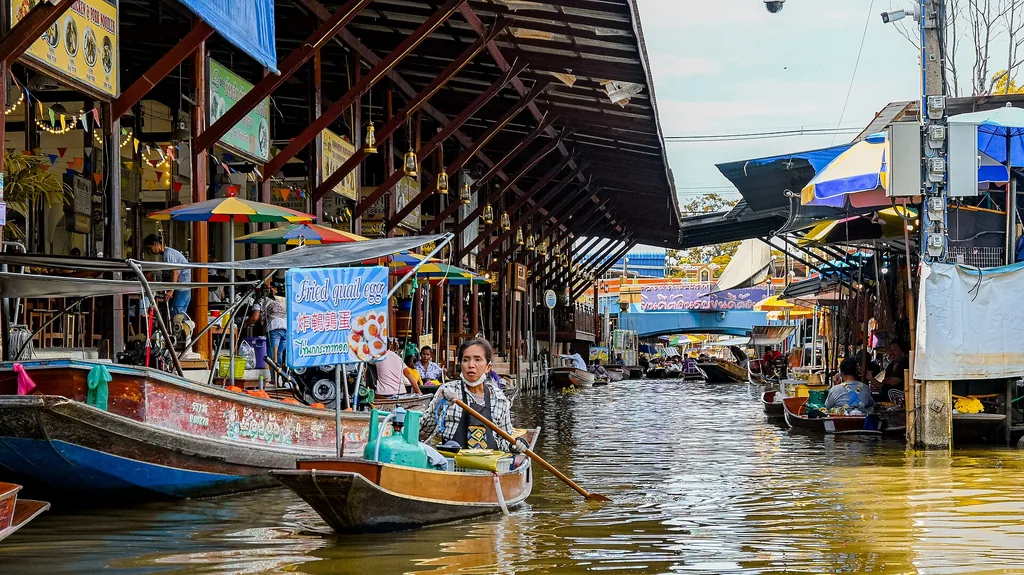 Thai vendor in a small wooden boat selling goods at Damnoen Saduak market